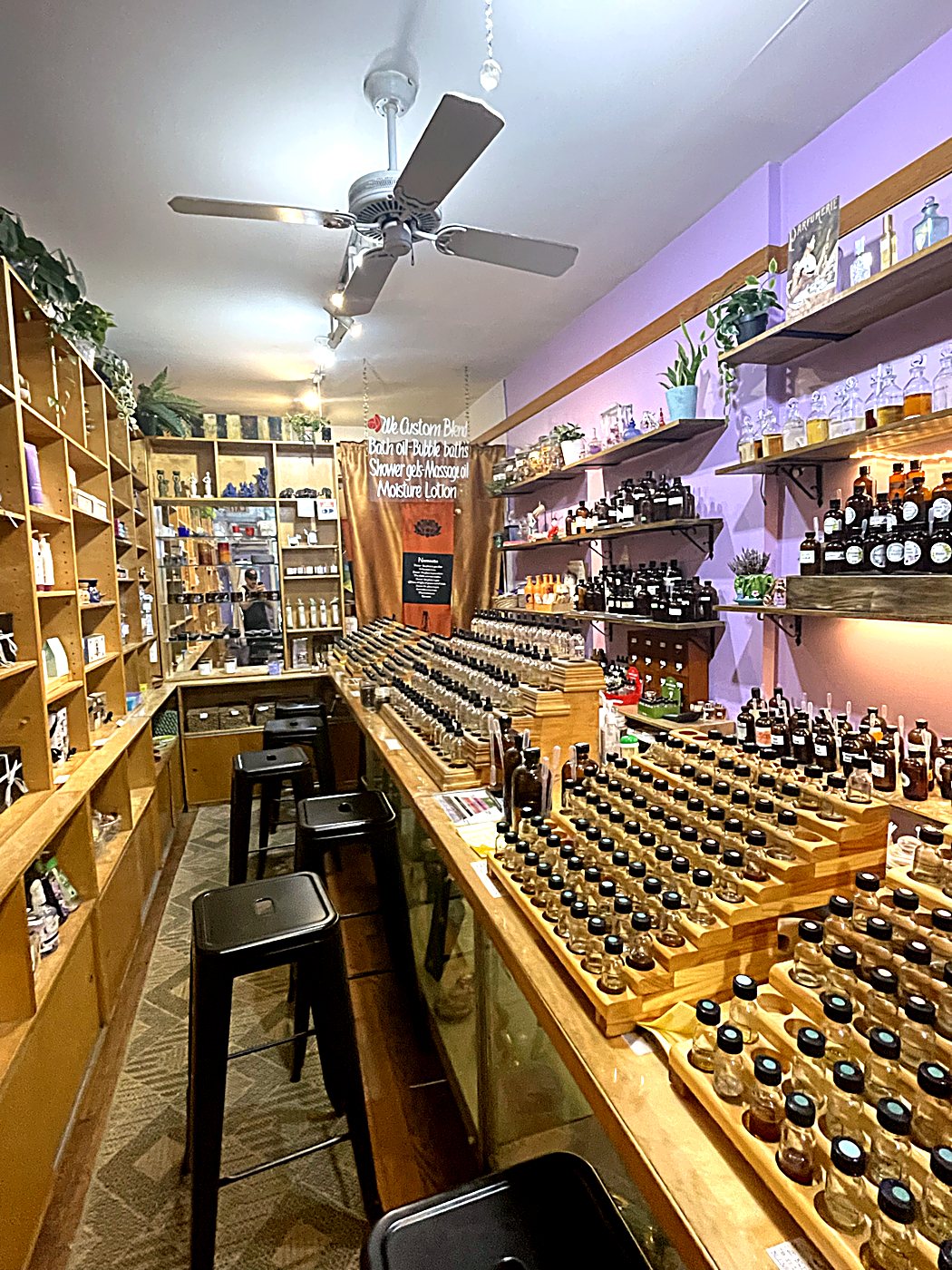 The narrow blending bar with six black stools, wooden shelves and hundreds of small bottles
