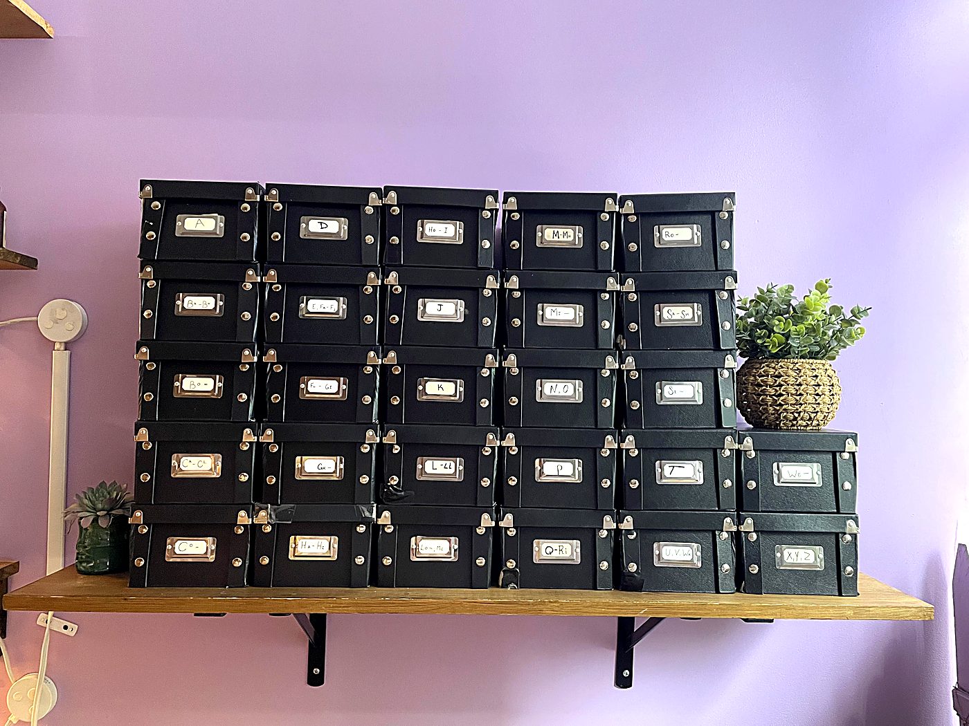 The Formula Library: alphabetized black archive boxes on a wooden shelf against the lavender wall