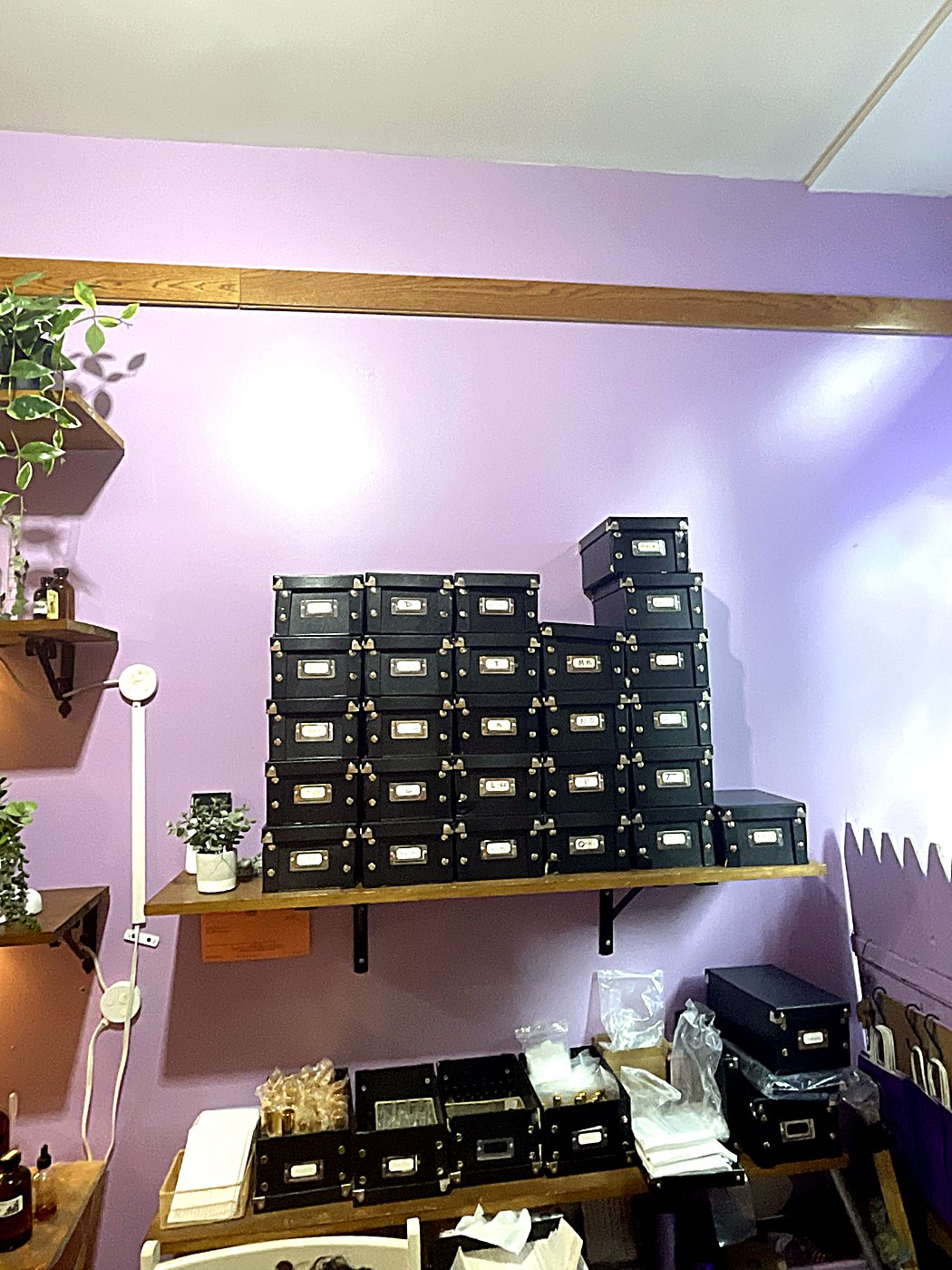 Shelves of black recipe boxes with brass label plates on a lavender wall